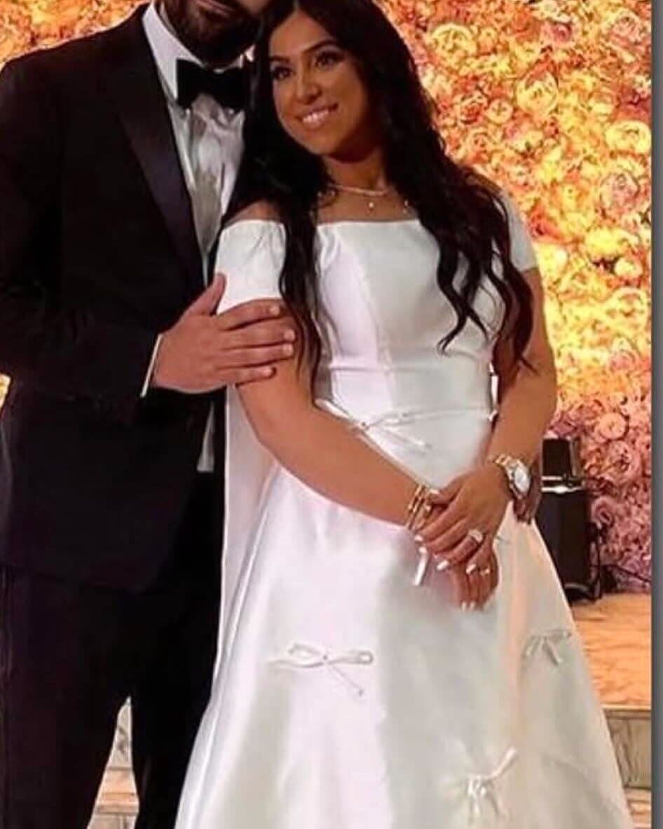 A bride in a satin gown with bow details beside her groom in a tuxedo