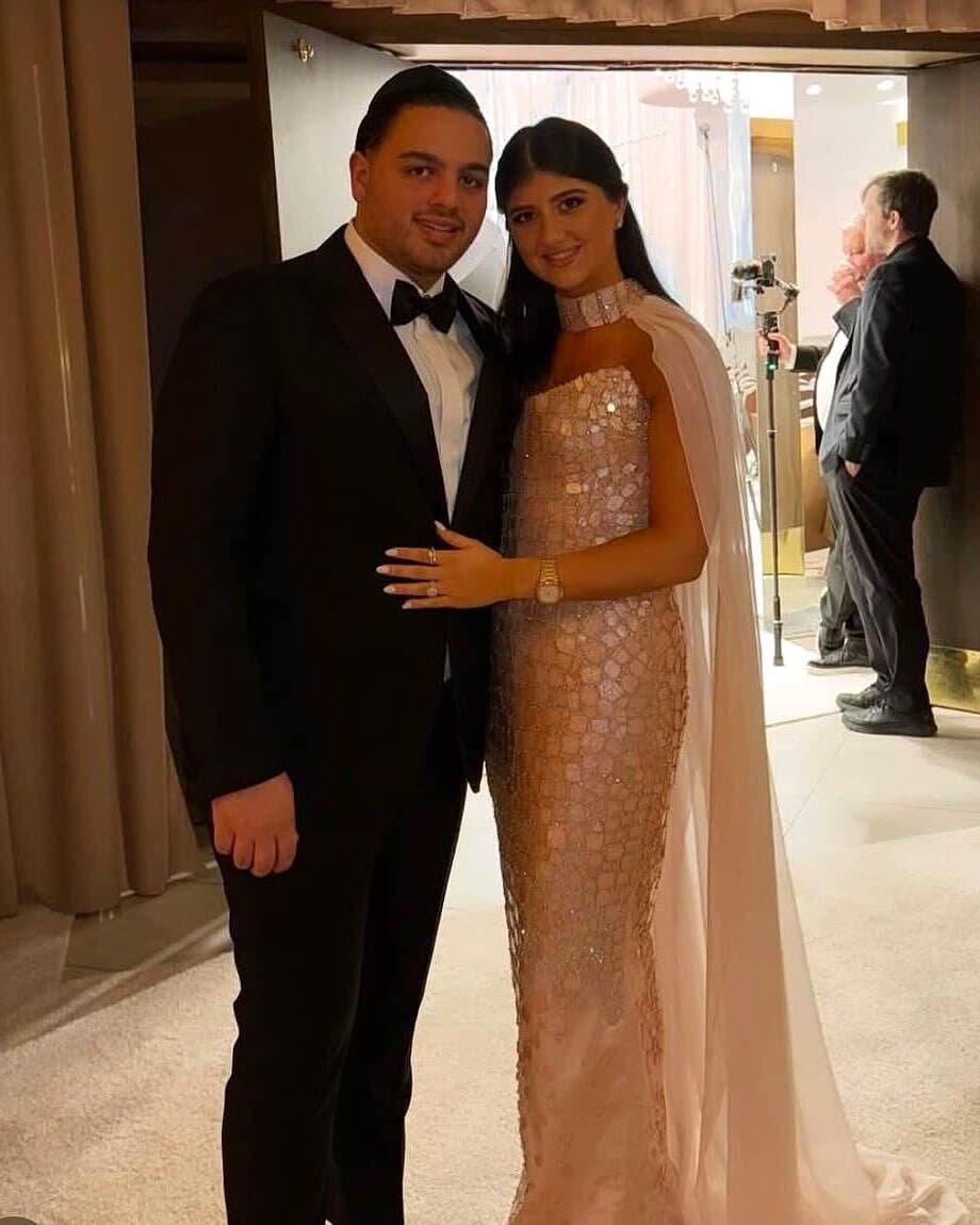 A bride in a sequined gown and cape with her groom at the reception