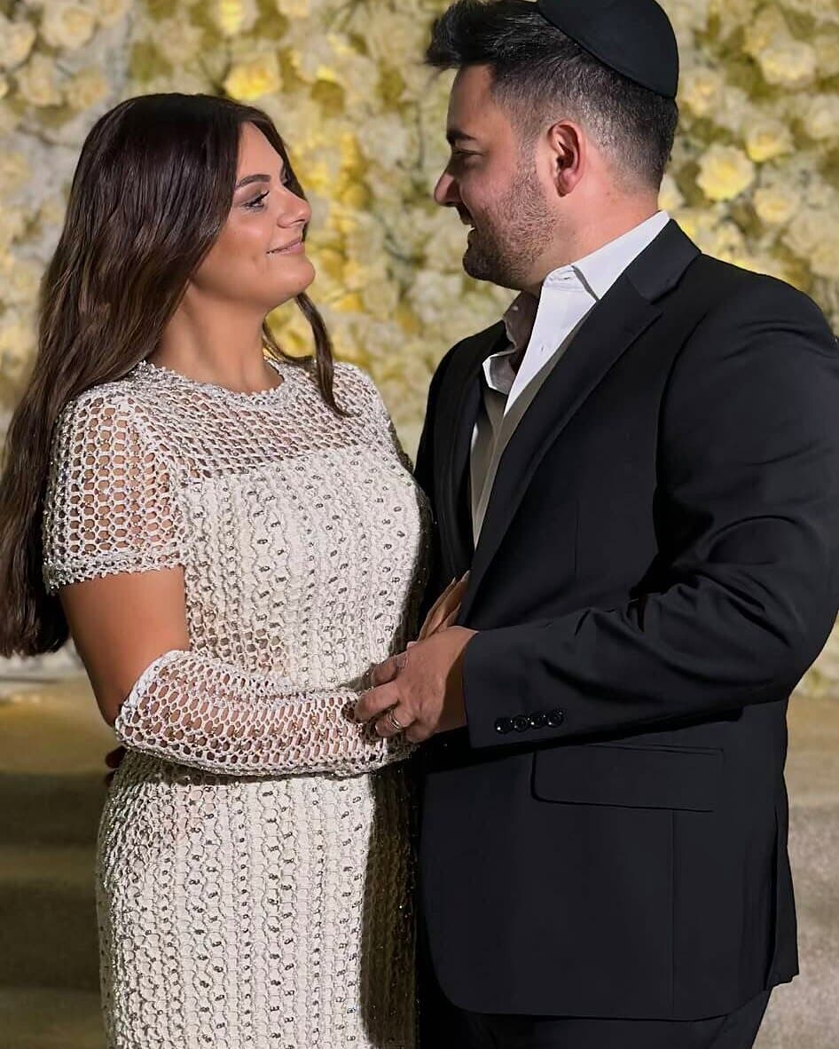 A newly engaged couple standing in front of a wall of white flowers