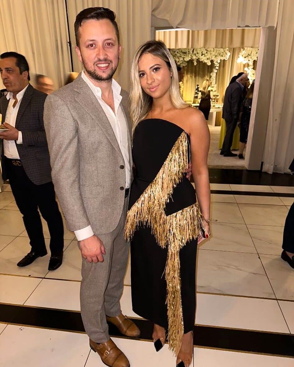 A couple at a wedding, she in a black gown with gold fringe